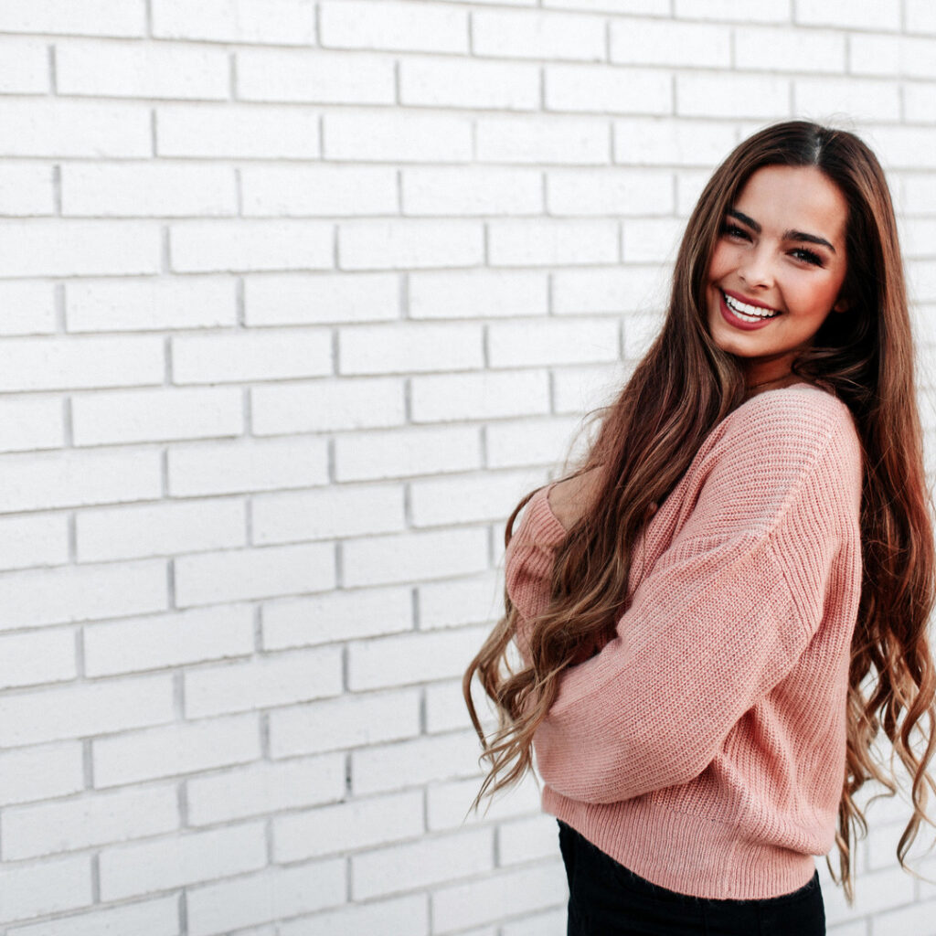 woman wearing pink sweater by a brick wall